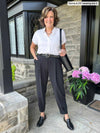 Miik founder Donna (five feet six, small) smiling wearing Miik's Nida pleat front tapered pant in graphite along with a short sleeve collared shirt in white 