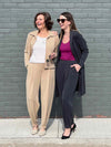 Miik founder Donna and Johanna smiling standing in front of a brick wall both wearing Miik's Nida pleat front tapered pant in the two colours available: wheat and graphite