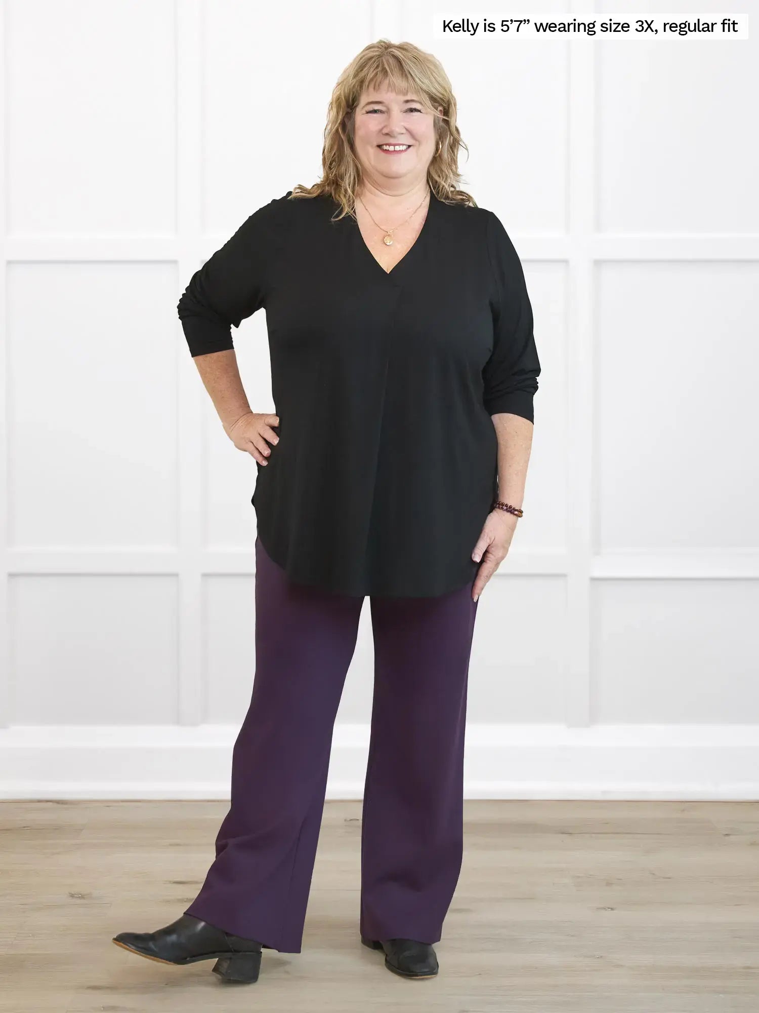 Woman wearing a black top and purple pants against a white background 