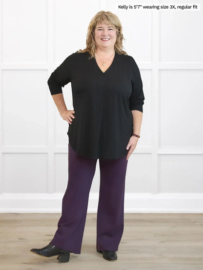 Woman wearing a black top and purple pants against a white background 