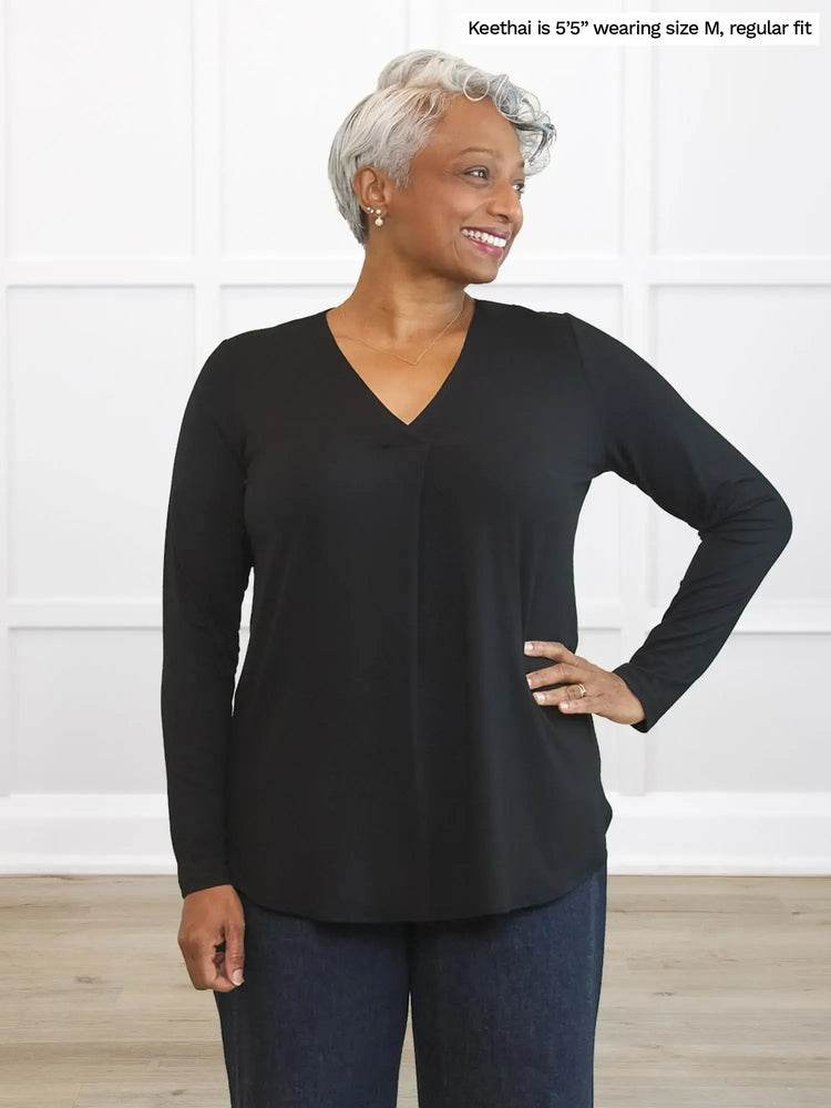 Woman wearing a black long-sleeve top and blue jeans against a white background 