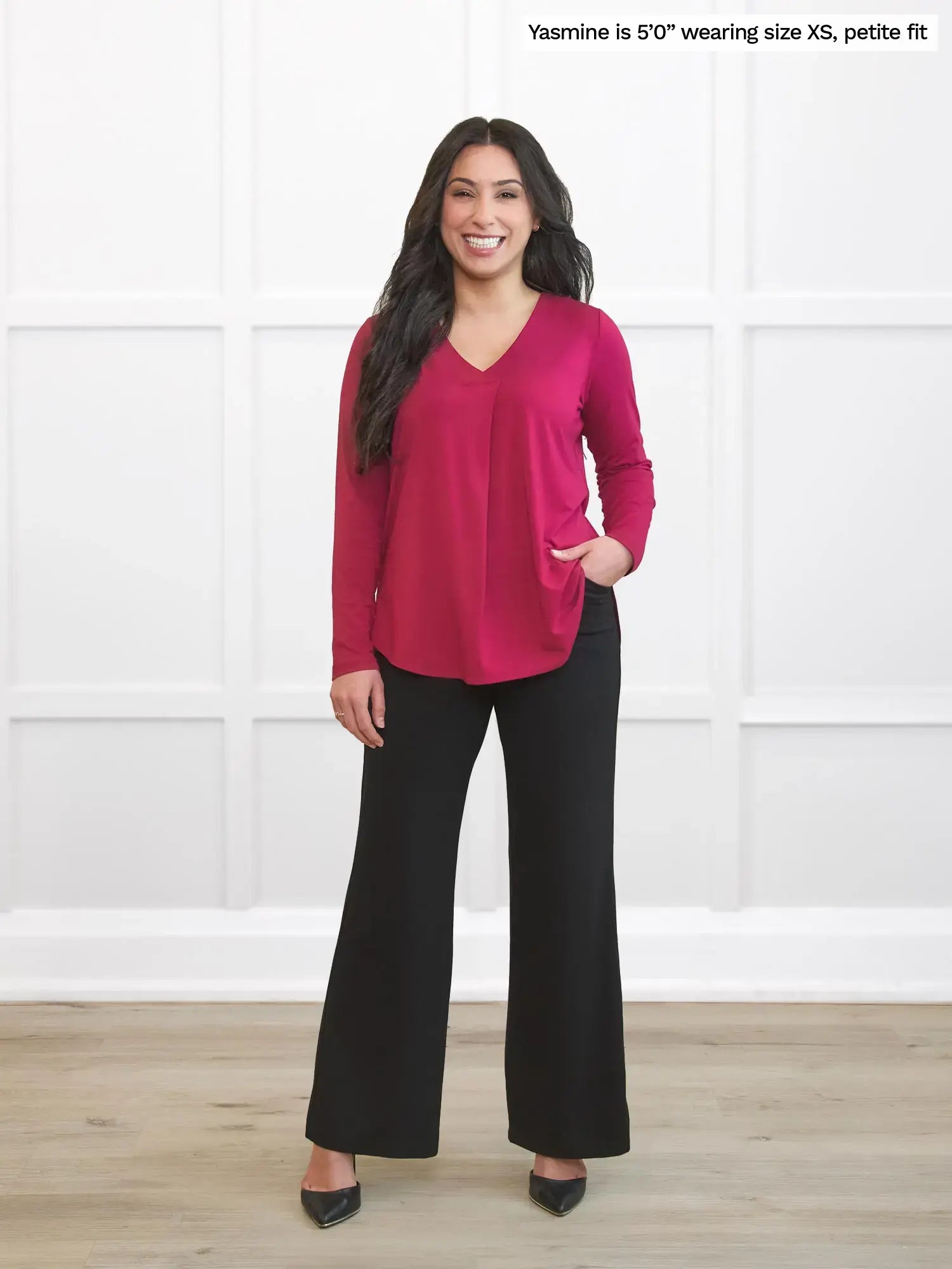 Woman wearing a red top and black pants against a white wall 