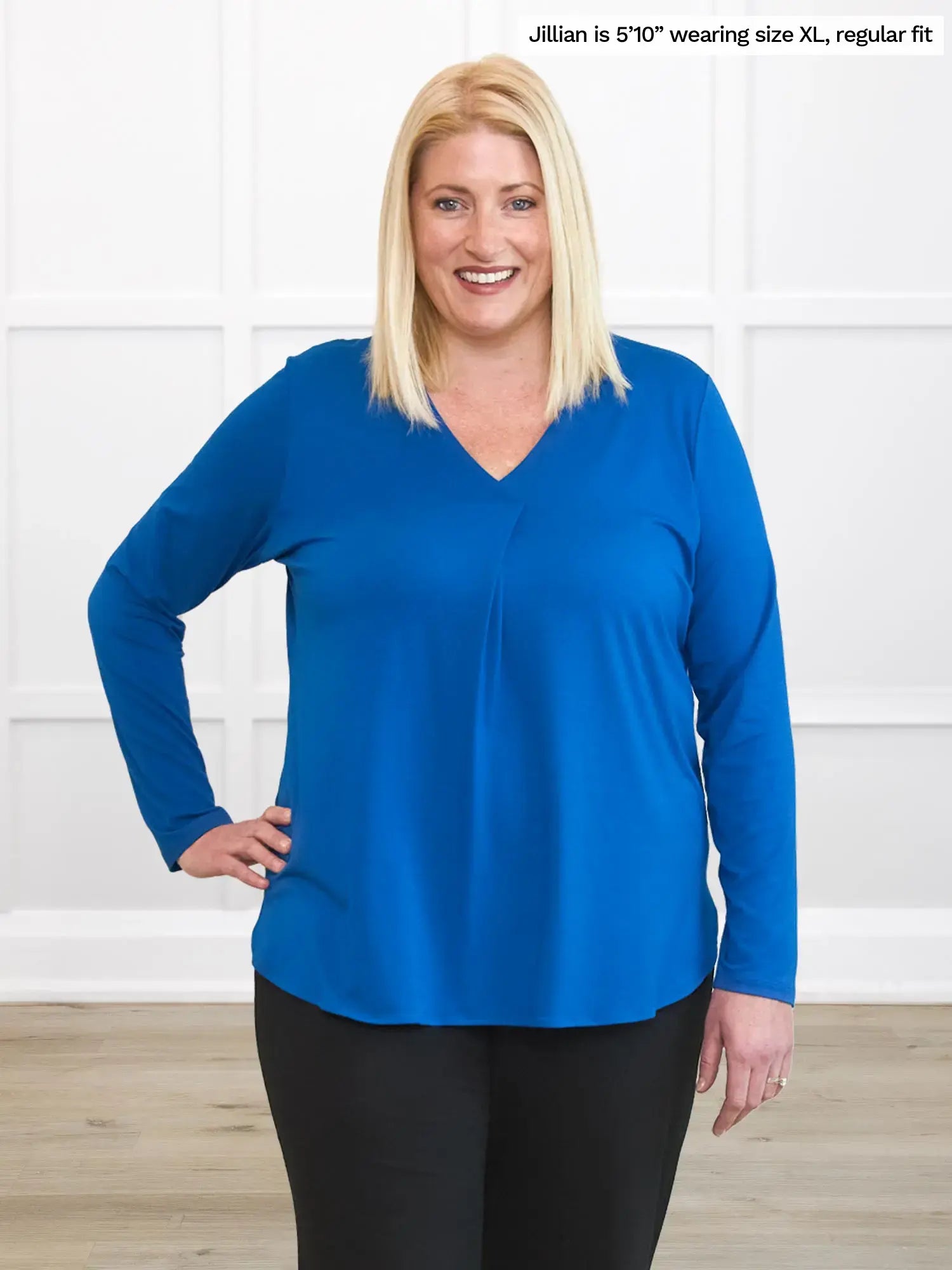 Woman wearing a blue long-sleeve top against a white wall. 