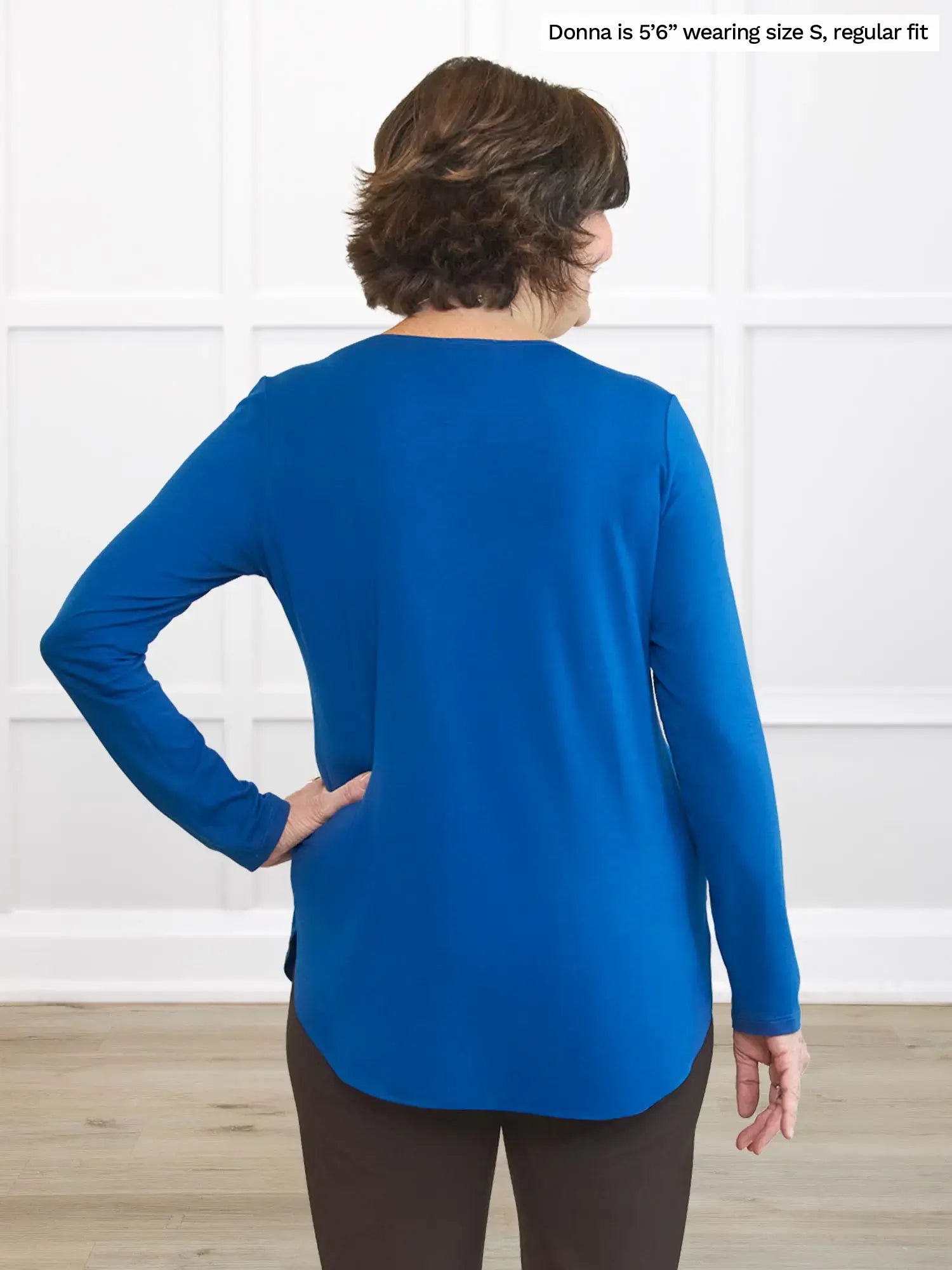 Back of person wearing a blue top and dark pants standing in front of a white wall 