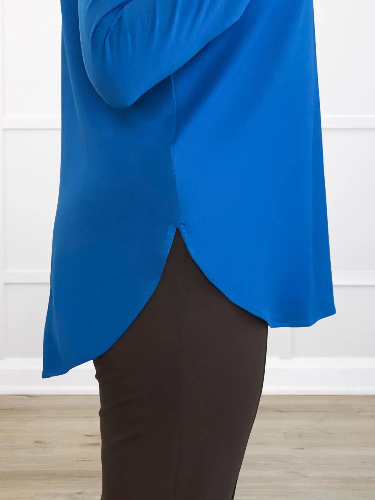 Closeup detail of a blue top with a side split hem against a white wall 