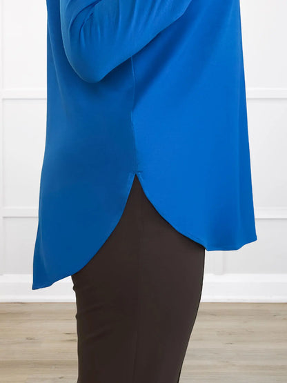Closeup detail of a blue top with a side split hem against a white wall 