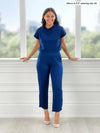 Miik model Meron (5'3", xsmall) smiling while standing in front of a window wearing Miik's Noah draped dolman top in ink blue with a capri tulip pant in the same colour