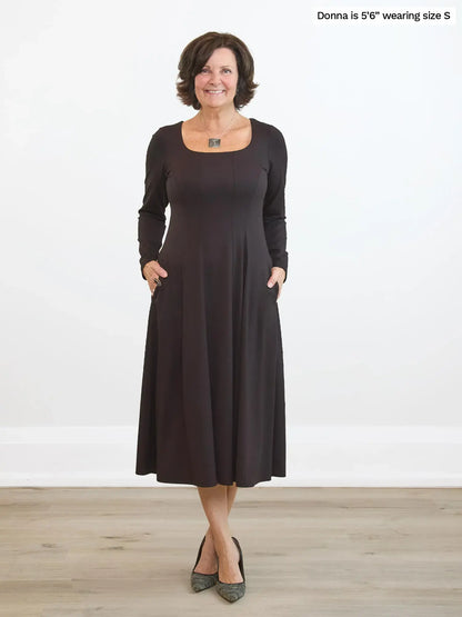 Woman wearing a dark brown dress standing on a wooden floor with a white background 