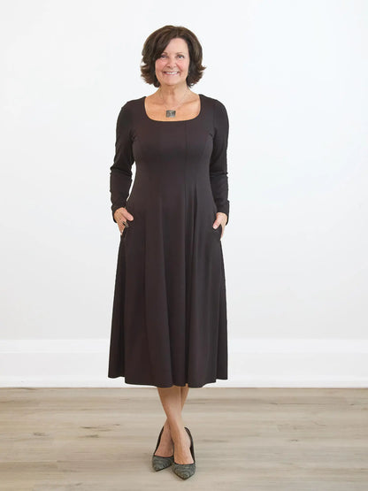 Woman wearing a dark brown dress standing on a wooden floor with a white background