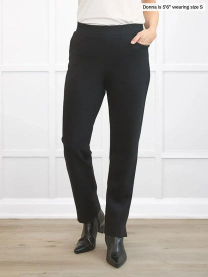 Person wearing black pants standing against a white wall. 