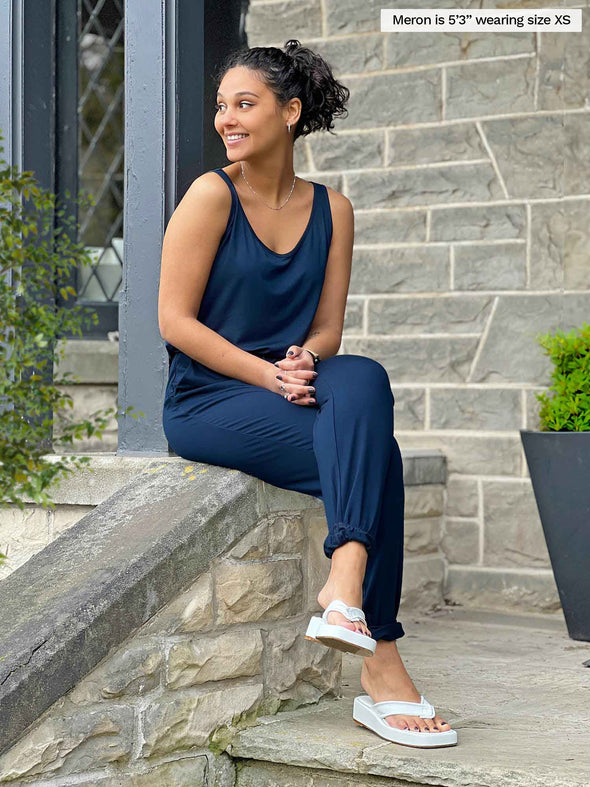 Miik model Meron (5'3", xsmall) siting and looking away wearing Miik's Perle open-back sleeveless jumpsuit in navy and white sandals 