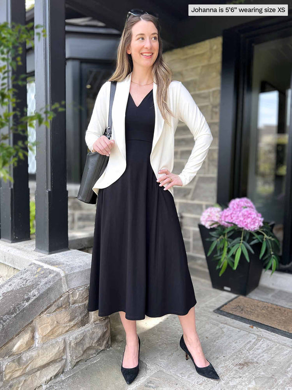 Miik model Johanna (five feet six, xsmall) standing in a front door of a house wearing Miik's RJ midi flounce dress with pockets in black with a natural soft blazer 