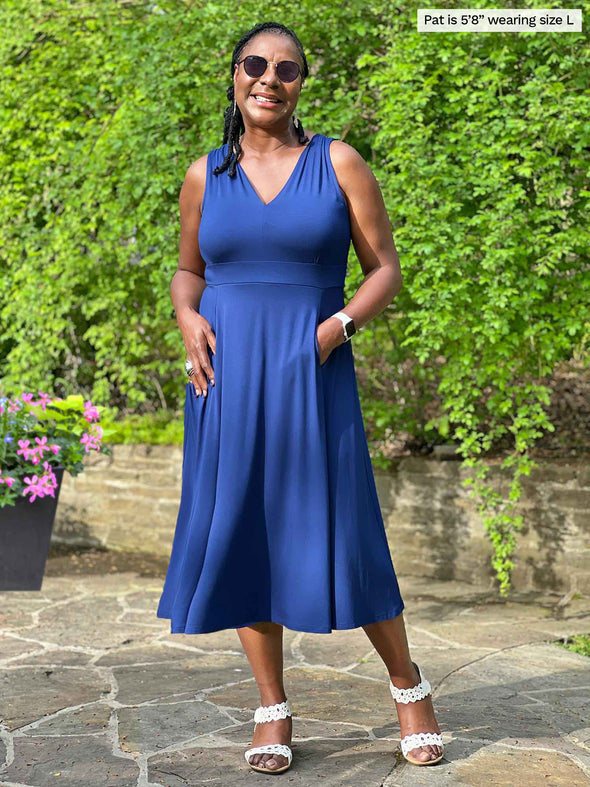 Miik model Pat (five feet eight, large) smiling wearing Miik's RJ midi flounce dress with pockets in blueberry and sunglasses 
