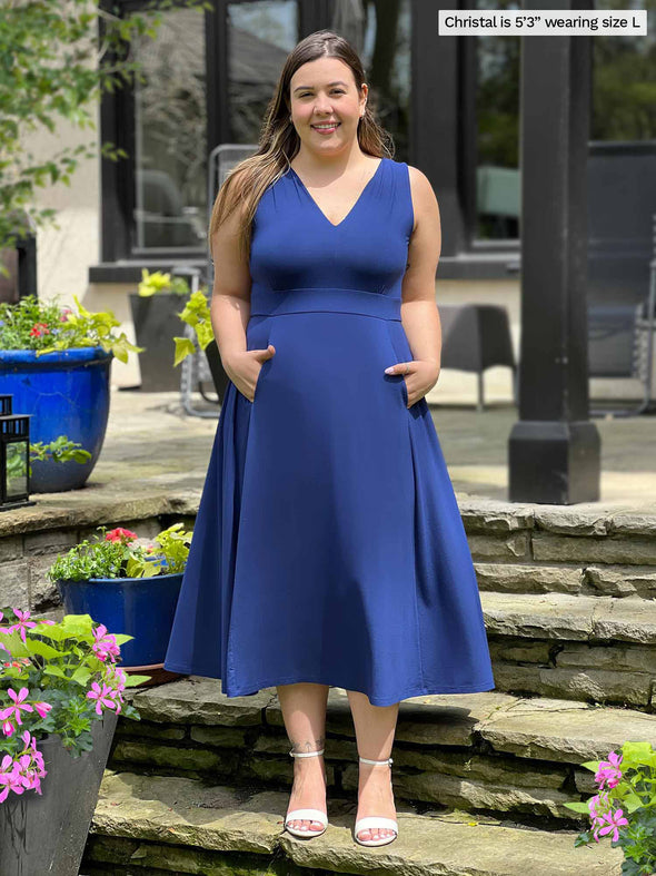 Miik model Christal (five feet three, large) smiling standing on the stairs of a backyard wearing Miik's RJ midi flounce dress with pockets in blueberry 