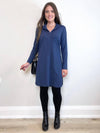 Woman standing in front of a white wall wearing Miik's Rafaela dressy collared tunic top in navy melange with black legging and boots