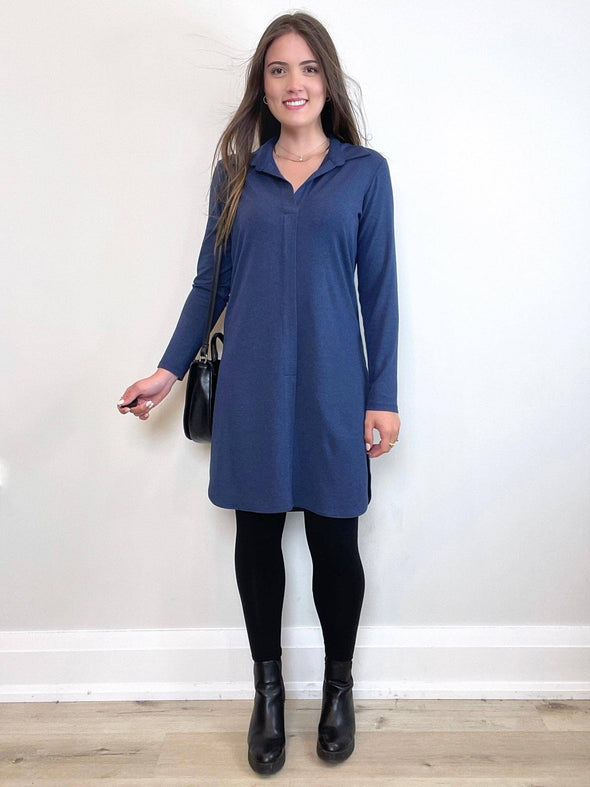 Woman standing in front of a white wall wearing Miik's Rafaela dressy collared tunic top in navy melange with black legging and boots