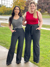 Two women standing on a sidewalk wearing Miik's Reed high waisted pant with pockets in charcoal pinstripe with a grey and red top.