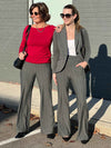 Two women smiling and looking away wearing Miik's Reed high waisted pant with pockets in granite wide pinstripe. One is wearing along with a long sleeve top in red wine, and the other one with a tank top in white and a charcoal blazer