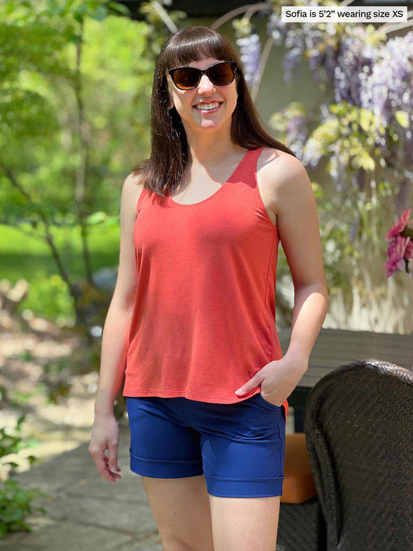Miik model Sofia (five feet two, xsmall) smiling wearing Miik's Reesa racerback high-low tank top in papaya melange along with a blueberry dressy short and sunglasses 