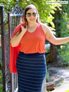 Miik model Christal (five feet three, large) smiling wearing Miik's Reesa racerback high-low tank top in papaya melange with a navy pinstripe midi skirt with a cardigan on her shoulders in the same colour of the tank top