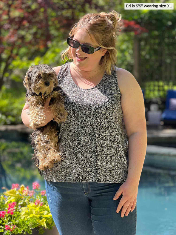 Miik model Bri (five feet five, xlarge) standing in front of a pool while holding a puppy wearing Miik's Reesa racerback high-low tank top in pebble with jeans