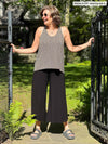 Miik founder Donna (five feet six, small) standing in the middle of a entryway wearing Miik's Reesa racerback high-low tank top in pebble with a wide leg capri pant in black