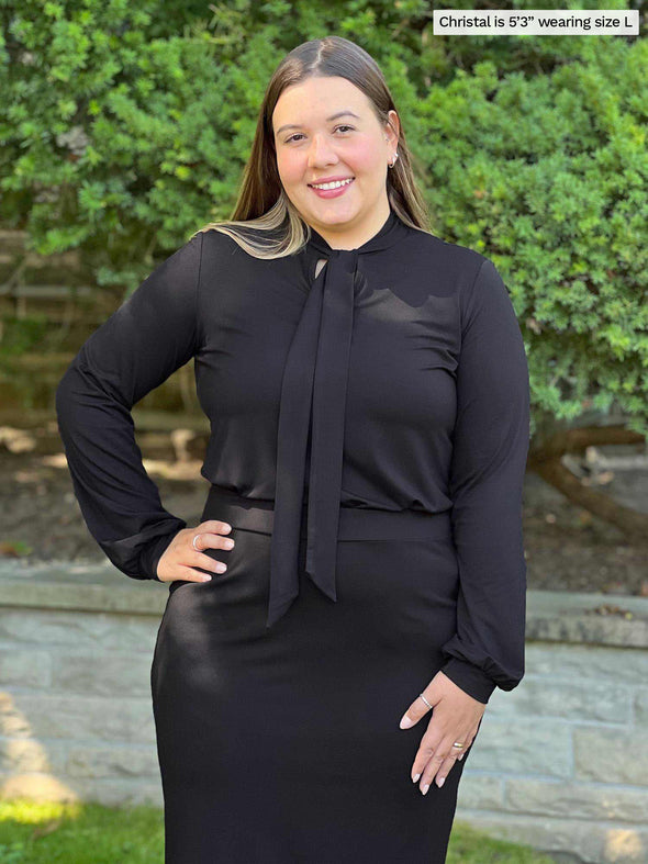 Miik model Christal (five feet three, large) wearing an all black outfit: Miik's Rhoda tie neck blouse with a pencil skirt