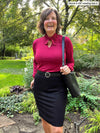Miik founder Donna (five feet six, small) standing in a backyard smiling wearing Miik's Rhoda tie neck blouse in bordeaux tucked in a pencil skirt in black with a belt