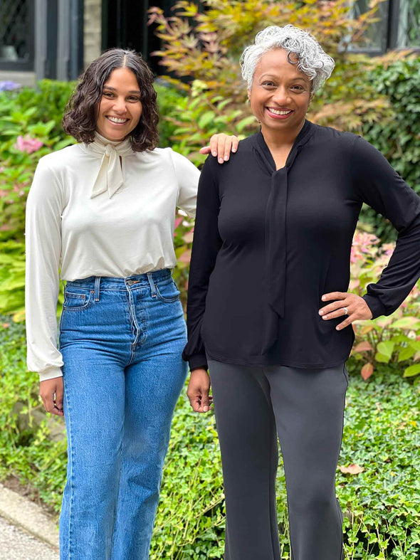 Miik models Keethai and Meron smiling both wearing Miik's Rhoda tie neck blouse. Meron is wearing in natural colour and Keethai in black