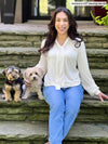 Miik model Yasmine (five feet tall, xsmall, petite) sitting on a backyard stairs next to two puppies wearing Miik's Rhoda tie neck blouse in natural with jeans 