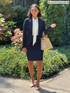 Miik model Meron (five feet three, xsmall) standing in front of a garden wearing a navy suit, Emily blazer and Jilly pencil skirt along with Miik's Rhoda tie neck blouse in natural