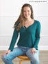 Woman wearing a teal long-sleeve shirt and blue jeans sitting on a wooden stool 