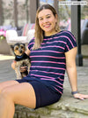 Miik model Christal (5'3", medium) smiling while sitting holding a puppy wearing Miik's Rio reversible dolman tee in beach house stripe with a navy shorts