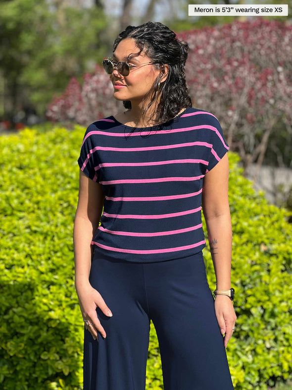 Miik model Meron (5'3" xsmall) looking away wearing Miik's Rio reversible dolman tee in beach house stripe with a navy wide leg pant and sunglasses
