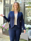 Miik model Andrea (5'10, large, tall) smiling wearing a navy suit - blazer and dress pant in the same colour, along with Miik's Rio reversible dolman tee in cobblestone print 
