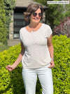 Miik founder Donna (5'6", small) smiling and looking away wearing a white jeans along with Miik's Rio reversible dolman tee in cobblestone print and sunglasses 
