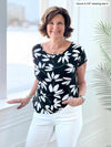 Miik founder Donna (5'6", small) standing in front of a window and smiling wearing a white jeans with Miik's Rio reversible dolman tee in white lily print 