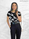 Woman standing in front of a wall wearing Miik's Rio reversible dolman tee in flower print and black pants.