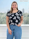 Woman standing in front of a window wearing Miik's Rio reversible dolman tee in flower print with jeans.