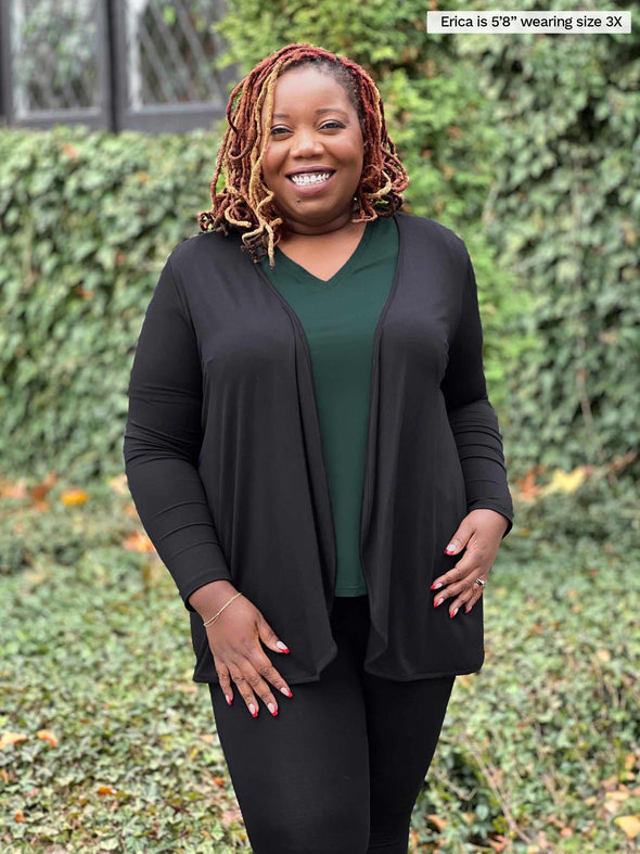 Miik model plus size Erica (5'8", size 2x) smiling wearing Miik's Rory waterfall cardigan in black with a legging in the same colour and a v-neck classic tee in pine green