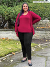 Miik model plus size Sureka (5'9", size 2x) smiling wearing a black pant along with Miik's Rory waterfall cardigan in bordeaux with a tank top in the same matching colour 