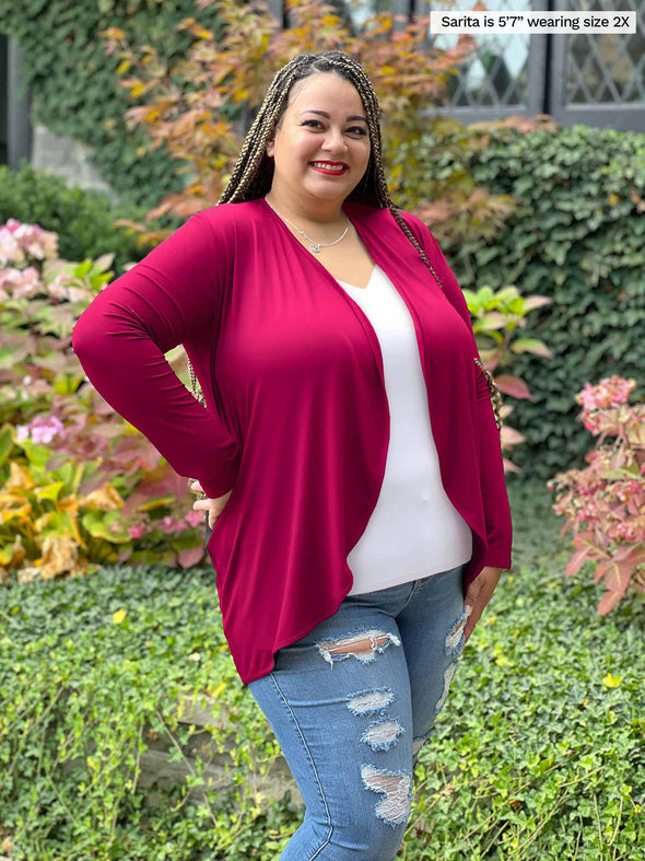 Miik model plus size Sarita (5'7", size 2x) smiling while standing sideway wearing a ripped jeans, a white v-neck classic tee along with Miik's Rory waterfall cardigan in bordeaux in a casual look