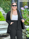 Miik model Christal (5'3", large) smiling wearing Miik's Rory waterfall cardigan in charcoal with pinstripe pant in the same colour and a white tank