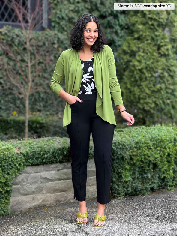 Miik model Meron (5'3", xsmall) smiling wearing Miik's Rory waterfall cardigan in green moss with a black pant and a printed tank