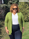 Miik model Carley (5'2, xxlarge) looking down and smiling wearing Miik's Rory waterfall cardigan in green moss with a white top and navy dress pant