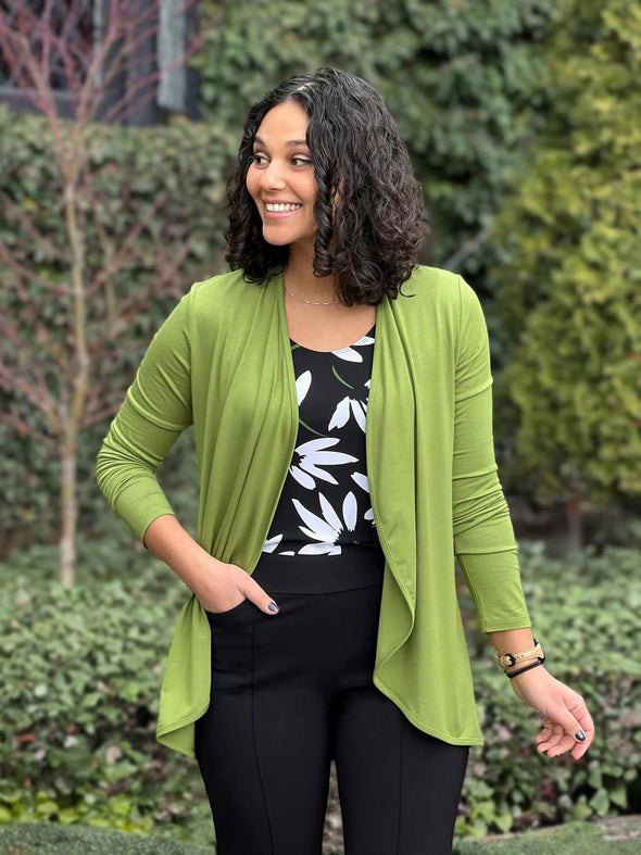 Miik model Meron (5'3", xsmall) looking away and smiling wearing Miik's Rory waterfall cardigan in green moss with a black pant and a printed tank