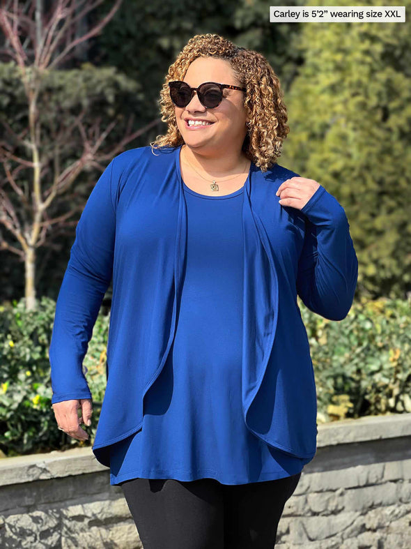 Miik model Carley (5'2", xxlarge) smiling wearing Miik's Rory waterfall cardigan in ink blue along with a tunic in the same matching colour and a black legging