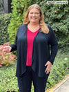 Miik model plus size Kelly (5'7", size 3x) smiling wearing Miik's Rory waterfall cardigan in navy with a matching colour dress pant and a bordeaux v-neck tee 
