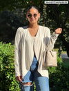 Miik model Meron (size XS, 5 foot 3) wearing Rory waterfall cardigan in oatmeal melange off-white over a matching tank top tucked into jeans.