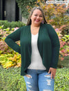 Miik model plus size Sarita (5'7", size 2x) smiling wearing Miik's Rory waterfall cardigan in pine green along with a white v-neck tee and ripped jeans